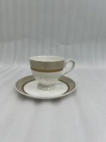 A luxury super bone china tea cup and saucer with gold pinstripe and laurel wreath patterns, filled with milk tea on a wooden table in a classic vintage living room setting with a fireplace and green armchairs