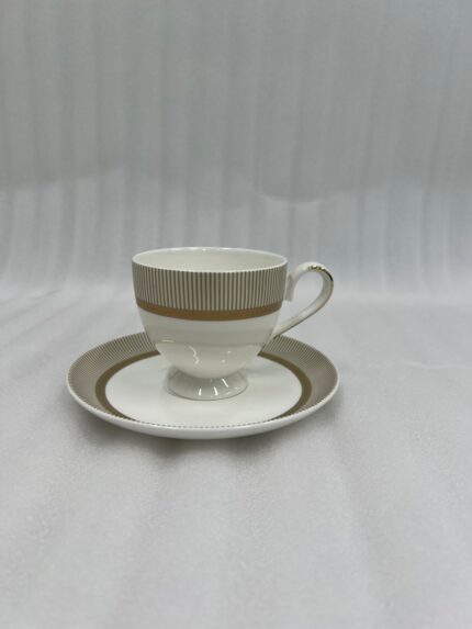 A luxury super bone china tea cup and saucer with gold pinstripe and laurel wreath patterns, filled with milk tea on a wooden table in a classic vintage living room setting with a fireplace and green armchairs