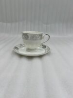A high-angle shot of a floral-patterned white bone china teacup filled with steaming tea, resting on a matching saucer on a polished wooden table in a luxurious library setting with a green velvet sofa and bookshelves