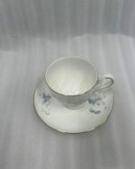 A steaming cup of black tea in a white bone china cup featuring blue floral patterns and a gold rim, resting on a matching saucer on a dark wooden table