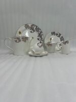 An elegant white and grey floral tea set on a wooden table, featuring a person pouring milk into a cup of tea alongside a plate of toasted rusks.
