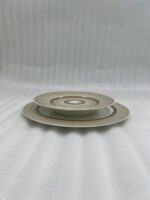 A stacked 18-piece super bone china plate set with a gold sunburst design on a wooden dining table.