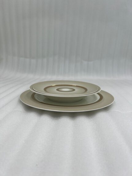 A stacked 18-piece super bone china plate set with a gold sunburst design on a wooden dining table.