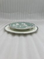 A stack of 18 super bone china plates featuring a sage green and white floral design, including rice plates, deep plates, and quarter plates, displayed on a white damask runner