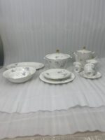 High-angle view of a 61-piece white super bone china dinner set with blue floral patterns and gold rims, elegantly arranged for an 8-person serving on a long mahogany dining table with blue chairs.