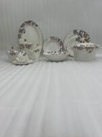 A luxury 61-piece Super Bone China dinner set with an intricate brown scroll pattern and gold accents, elegantly arranged for an 8-person serving on a white tablecloth under a crystal chandelier