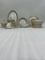 A premium 61-piece Super Bone dinner set by OneMore Crockery featuring cream-colored plates with gold-rimmed textured borders, including a teapot, cups, serving bowls, and platters arranged on a dark wooden table