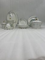 A luxury 61-piece Super Bone China dinner set with blue floral patterns and silver rims displayed on a wooden dining table, including plates, bowls, a teapot, and a serving casserole.