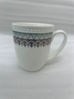 A premium bone china mug filled with hot tea on a black marble countertop, featuring a turquoise geometric pattern and silver lace design, set against a cozy kitchen background with soft natural lighting