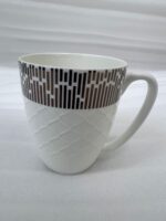A steaming cup of green tea in a white bone china mug with a bronze geometric pattern and embossed lattice texture, sitting on a wooden table