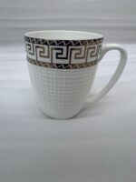 A close-up of a steaming mug of tea with a white and gold Greek Key pattern on a wooden table, part of a 6-piece Bone China mug set
