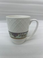 A close-up shot of a white bone china mug filled with tea, resting on a slate coaster on a rainy balcony railing. The mug features an embossed diamond pattern and a decorative floral band at the bottom