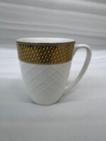 A set of elegant white bone china mugs with an embossed diamond pattern and a golden basket-weave rim, filled with steaming hot tea on a wooden table.