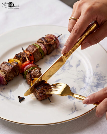 High-angle studio shot of a 36-piece gold-plated cutlery set arranged on a polished wooden surface, featuring matching serving pieces, dinner spoons, forks, knives, and teaspoons with elegant handle detailing.