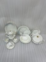 An elegant white super bone china dinner set with gold rims and a delicate grey leaf pattern, displayed on a wooden table