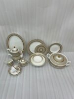 An elegant super bone china dinnerware set featuring a fine beige and gold-lined sunburst pattern, arranged neatly on a wooden table. The collection includes dinner plates, an oval platter, a tureen with a lid, soup bowls, a teapot, a creamer, a sugar bowl, and a teacup with a saucer
