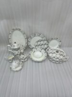 An elegant white and grey floral patterned super bone china dinner set arranged on a wooden table, including plates, bowls, a teapot, a casserole dish, and teacups.