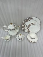 Elegant super bone china tea set featuring a teapot, teacup, plates, cream pitcher, and sugar bowl with a brown vintage baroque pattern and gold rims, displayed on a wooden table.