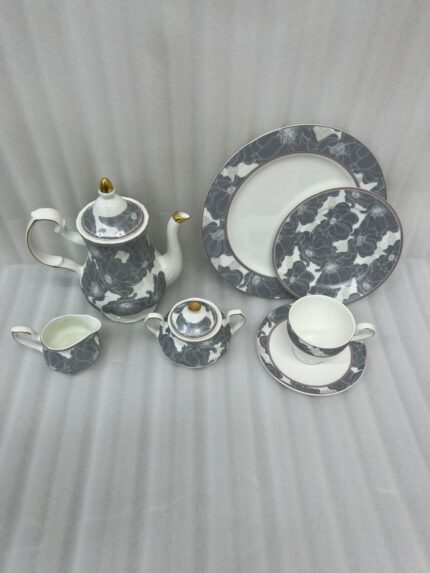 A premium grey and white floral pattern super bone china tea set featuring a teapot with gold accents, a creamer, a sugar bowl, plates, and a filled teacup with a saucer on a wooden table.
