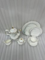Luxury super bone china tea set featuring a teapot, teacup, saucer, creamer, and sugar bowl with fine gold trim and soft grey feather patterns on a wooden table.