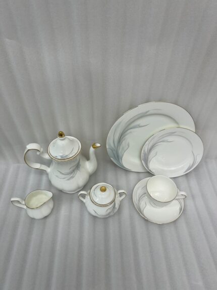 Luxury super bone china tea set featuring a teapot, teacup, saucer, creamer, and sugar bowl with fine gold trim and soft grey feather patterns on a wooden table.
