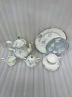 A premium super bone china tea set featuring a classic teapot, sugar bowl, creamer, teacup with saucer, and matching plates, all adorned with an elegant light blue and grey floral pattern on a wooden table.