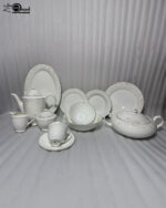A comprehensive 61-piece super bone china dinner set arranged for display against a neutral textured background. The white porcelain tableware features a delicate cream and gold floral pattern on the rims. The collection includes dinner plates, side plates, soup bowls, a large oval platter, a lidded serving tureen, a teapot with matching sugar bowl and creamer, and teacups with saucers