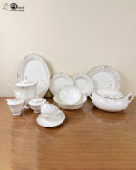 Detailed product photograph of an elegant 61-piece super bone china dinner set for 8-person serving, displayed on a polished wooden surface. The set includes a full tea service (teapot, creamer, sugar bowl, teacup and saucer), multiple plates and bowls, a large lidded tureen, and various serving pieces, all featuring delicate light gold damask filigree patterns and gold trim on a cream-white surface. The 'one more' brand logo is visible in the upper left corner.