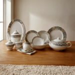 An elegant 61-piece premium super bone china dinner set with grey and gold marbled rims displayed on a warm wooden tabletop, featuring luxury plates, bowls, a covered tureen, and a teapot setup