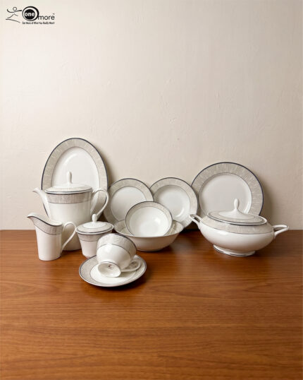 An elegant 61-piece white super bone china dinner set arranged on a polished wooden table against a neutral beige wall. The porcelain tableware features sophisticated silver-grey textured borders and includes dinner plates, bowls, a large oval serving platter, a covered soup tureen, and a complete tea service with a teapot, creamer, sugar bowl, cups, and saucers