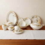 An elegant 61-piece One More brand super bone china dinnerware set with gold rims and soft floral patterns, arranged beautifully on a wooden table with a white runner