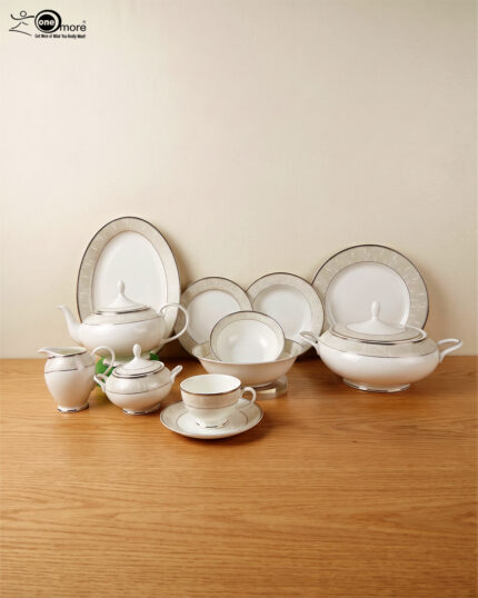 An elegant 61-piece super bone china dinnerware set for an 8-person serving, featuring white plates, bowls, a teapot, a covered tureen, and teacups with detailed beige and silver patterned rims, neatly arranged on a wooden table