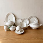 Elegant 61-piece super bone china dinner set by OneMore with an intricate silver lace border design, beautifully arranged on a wooden table against a plain background, including plates, bowls, a teapot, and a soup tureen