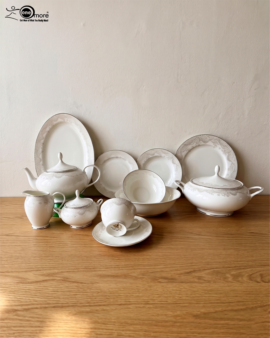 2 Elegant 61-piece super bone china dinner set by OneMore with an intricate silver lace border design, beautifully arranged on a wooden table against a plain background, including plates, bowls, a teapot, and a soup tureen