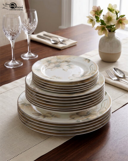 A beautifully stacked 18-piece premium Super Bone China plate set featuring an elegant floral pattern and fine trim, arranged on a beige linen table runner alongside crystal wine glasses and a rustic flower vase.