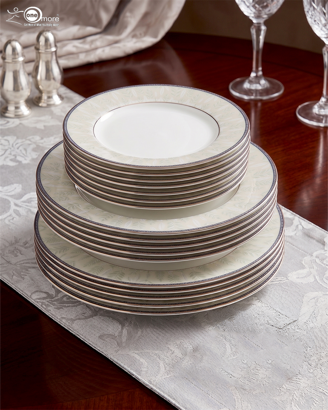 2 A professionally styled stack of the OneMore 18-piece super bone china dinnerware set, showcasing six quarter plates on top, six deep plates in the middle, and six large rice plates at the bottom, featuring an elegant light-green patterned border on a silver table runner