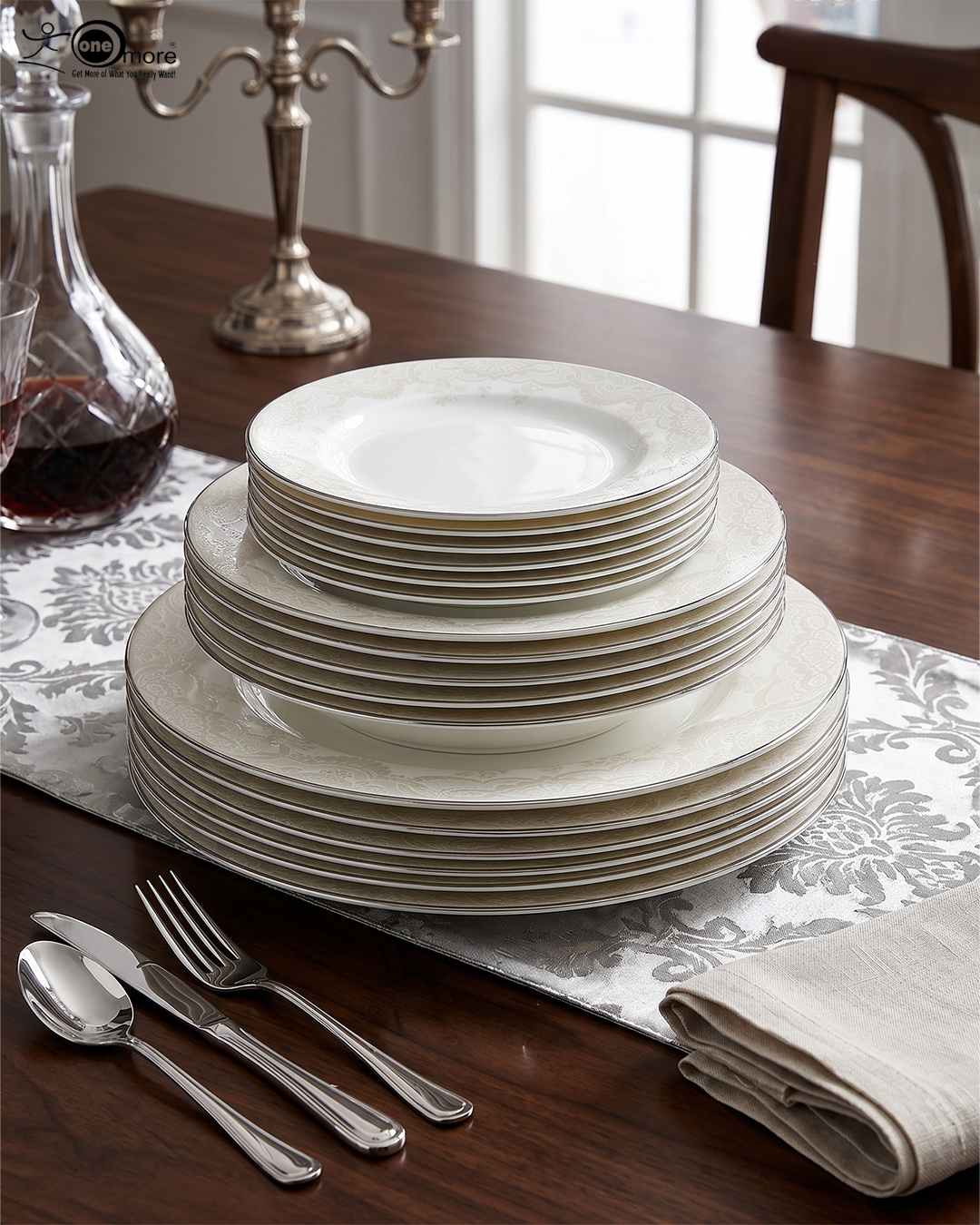 2 A stacked 18-piece OneMore super bone china dinnerware plate set featuring elegant cream plates with intricate lace damask borders, displayed on a dark wooden table with a silver runner and stainless steel cutlery
