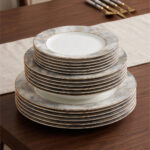 A stacked 18-piece super bone china dinnerware set featuring a modern grey and gold marble pattern with elegant gold rims, neatly displayed on a wooden dining table alongside luxury cutlery.