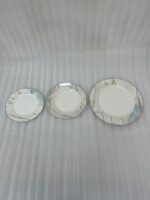 A neatly stacked 18-piece super bone china dinner plate set featuring a white and mint green marble pattern with gold veining, arranged on a dining table with silverware and a crystal glass.
