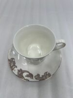 A luxury white super bone china cup and saucer featuring gold leaf designs and a gold rim, set on a white placemat on a wooden dining table.