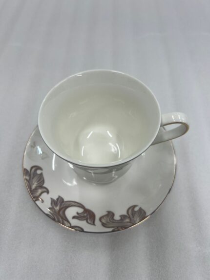 A luxury white super bone china cup and saucer featuring gold leaf designs and a gold rim, set on a white placemat on a wooden dining table.