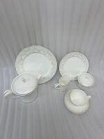 A complete 24-piece white porcelain tea set featuring delicate lace-patterned edges and silver trim, arranged on a wooden table.