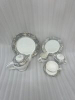 A 24-piece porcelain tea set featuring a modern grey marble pattern border with silver accents, including a teapot, milk pot, sugar bowl, cups, saucers, and plates arranged on a wooden surface.