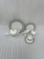 A 24-piece luxury porcelain tea set featuring a crisp white finish, sophisticated grey floral patterned rims, and delicate gold accents, arranged on a glossy surface.