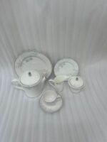 A sophisticated 24-piece white porcelain tea set featuring a delicate grey floral pattern and silver trim, arranged elegantly on a table runner.