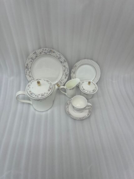 A 24-piece luxury porcelain tea set featuring a delicate blue floral pattern, gold accents, and striped borders, arranged elegantly on a linen runner.