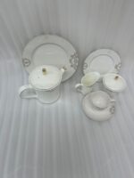 A complete 24-piece porcelain tea set featuring a teapot, sugar bowl, milk jug, tea cups, saucers, and plates, all decorated with intricate grey filigree patterns and gold accents, displayed on a marble surface.