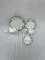 A 24-piece luxury porcelain tea set featuring a delicate blue floral pattern with gold trim, including a teapot, cups, saucers, plates, and serving accessories on a wooden table.