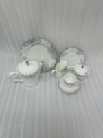 A complete 24-piece luxury porcelain tea set featuring a delicate blue floral pattern on white china with silver rims, displayed on a wooden table.