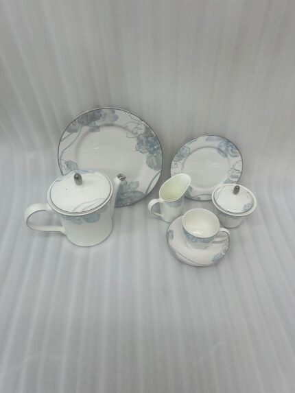 A complete 24-piece luxury porcelain tea set featuring a delicate blue floral pattern on white china with silver rims, displayed on a wooden table.